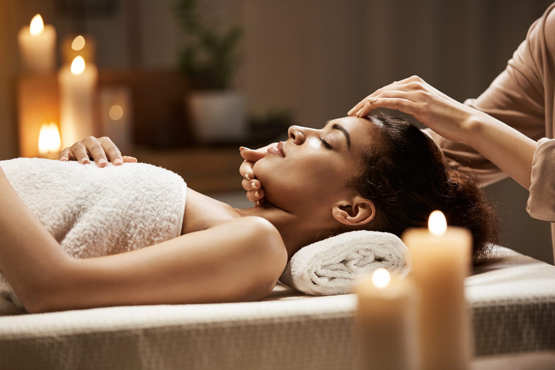 Attractive african girl enjoying face massage in spa salon.